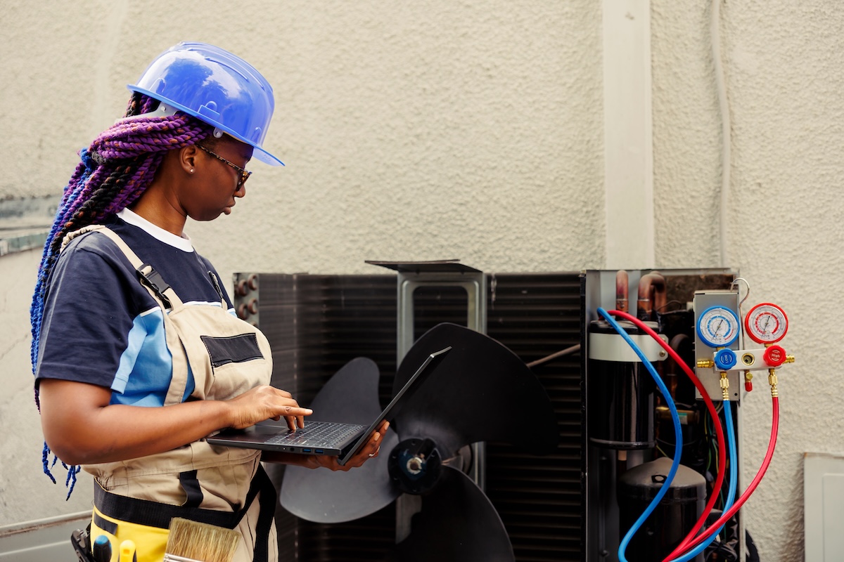 Licensed efficient electrician commissioned for leaks checking, making sure all hvac system vents are clear of waste. Precise serviceman doing air conditioner inspection, imputing data on laptop