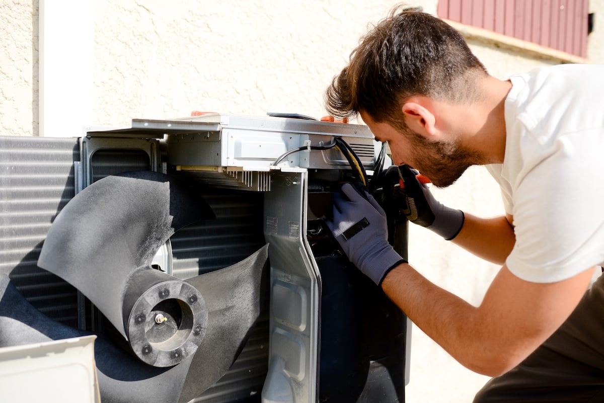 young man electrician installer working on outdoor compressor unit air conditioner at a client's home