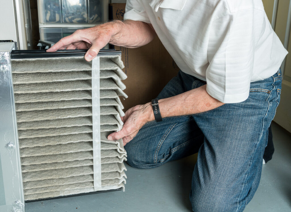 how often to change furnace filter Senior caucasian man changing a folded dirty air filter in the HVAC furnace system in basement of home