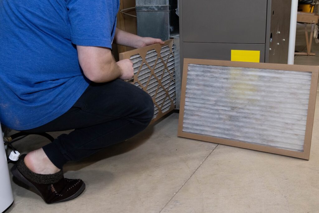 how often to change furnace filter homeowner preforming general maintenance on home furnace, replacing the old dirty filter with a clean fresh filter for better air flow
