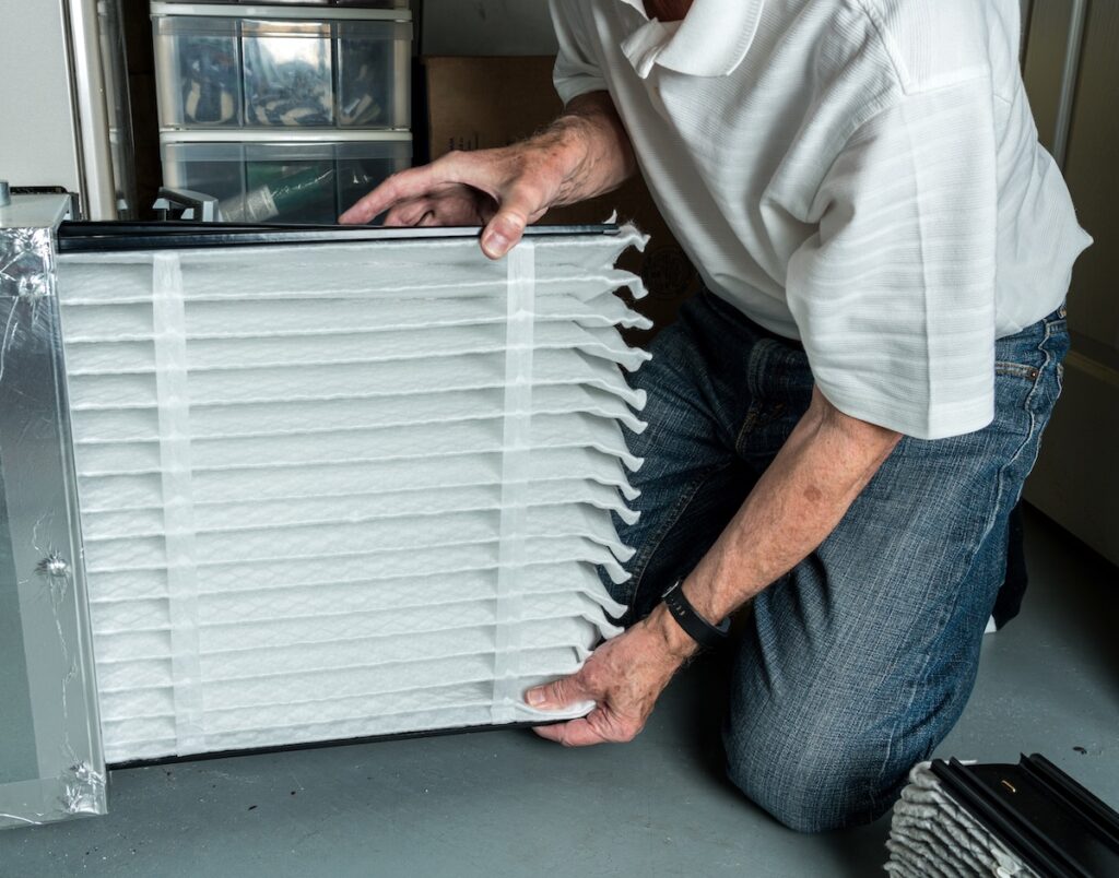 best furnace filters Senior caucasian man checking a clean folded air filter in the HVAC furnace system in basement of home