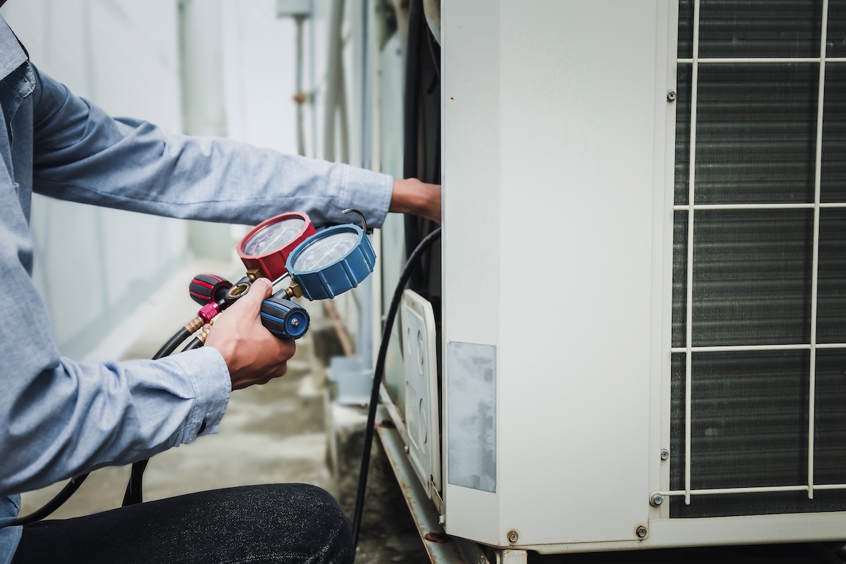 Mechanic air conditioner technician is using a manifold gauge to check the refrigerant in the system to inspect and repair the outdoor air compressor.