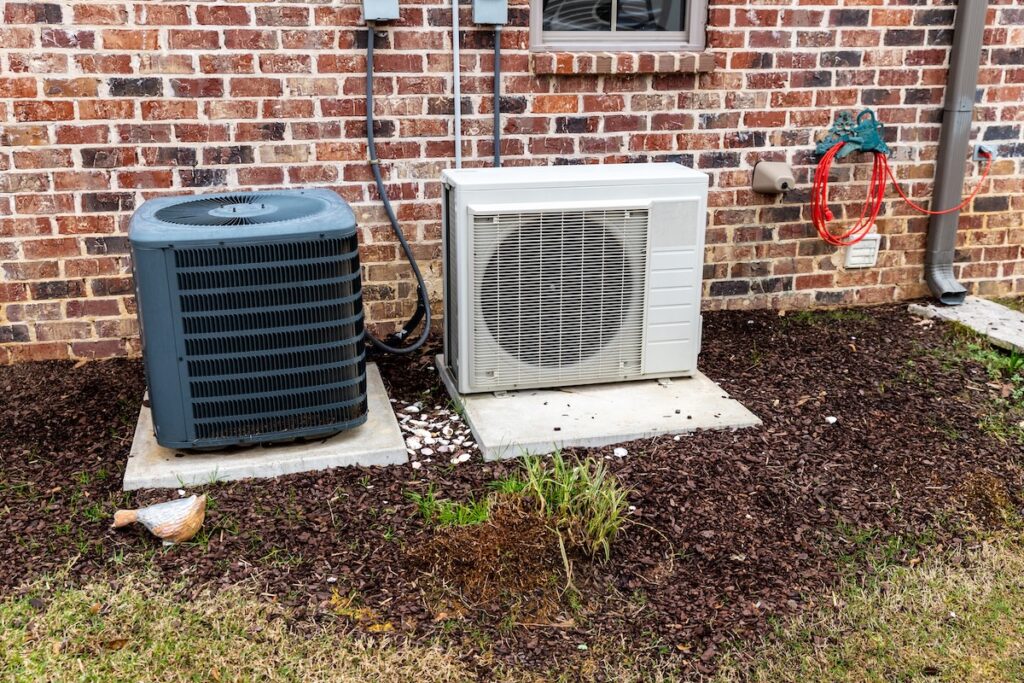 mini split vs central air HVAC Air Conditioner Compressor and a Mini-split system together next to each other, next to a brick home.