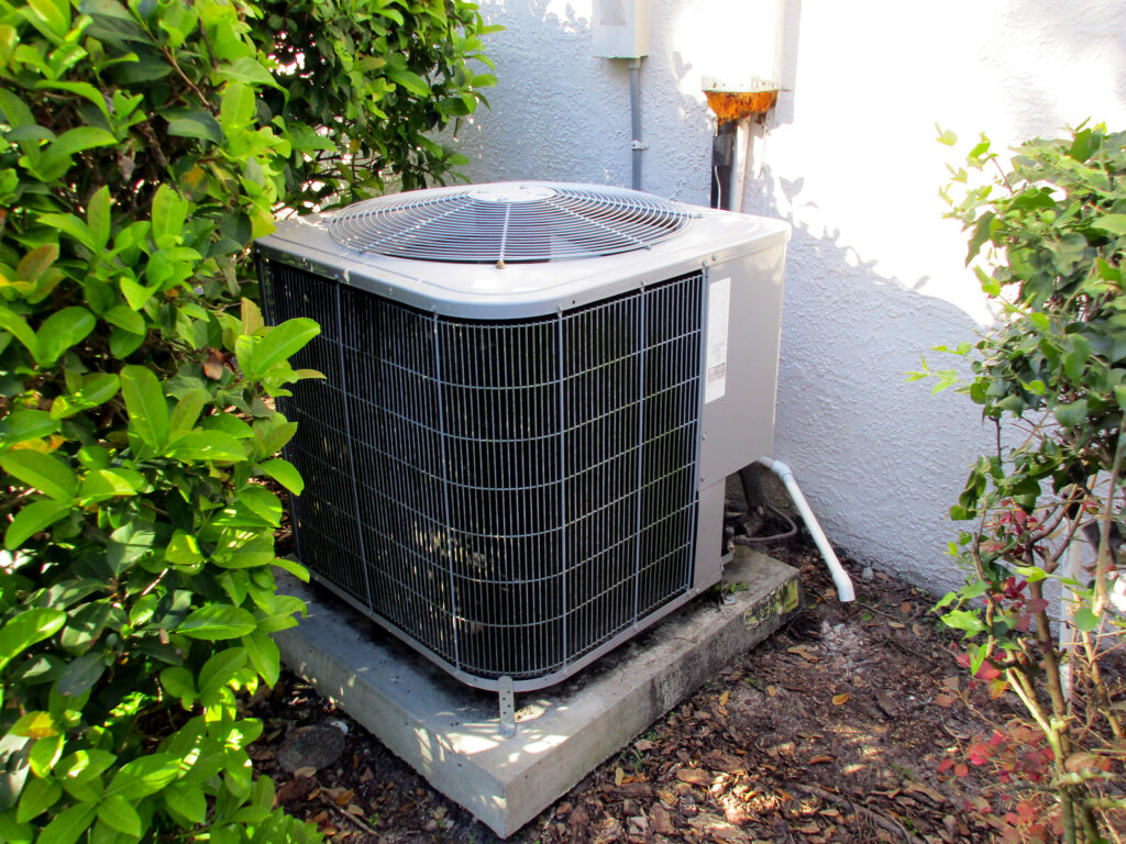A professionally leveled AC condenser unit nestled near lush green landscaping, highlighting the meticulous outdoor site prep and custom central air installation.