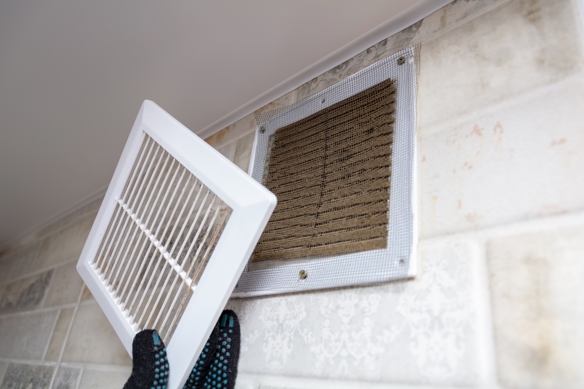 repair service man removing a dirty air filter on a house so he can replace it with a new clean. Extremely dirty and dusty white plastic ventilation air grille at home close up, harmful for health