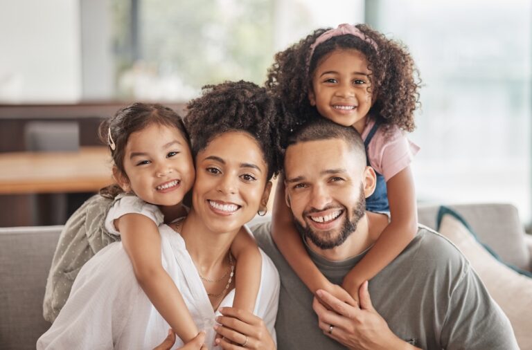 Happy, smile and portrait of an interracial family sitting on a sofa in the living room at home. Happiness, love and adoptive parents bonding, embracing and relaxing with their children in the lounge.
