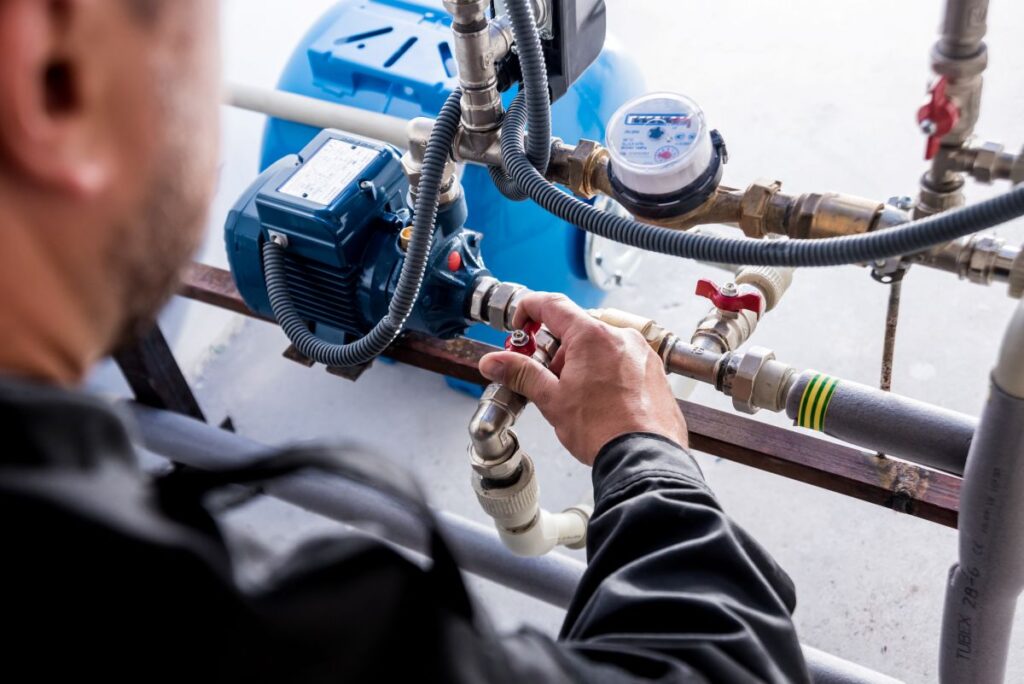 backflow testing technician repairing and adjusting water pipes outside of family house