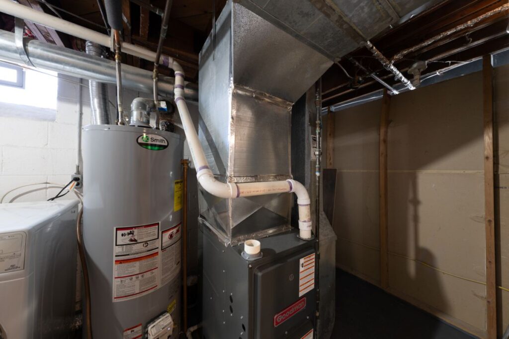 A basement utility room featuring a modern high-efficiency gas furnace with complex ductwork installed alongside a residential water heater.