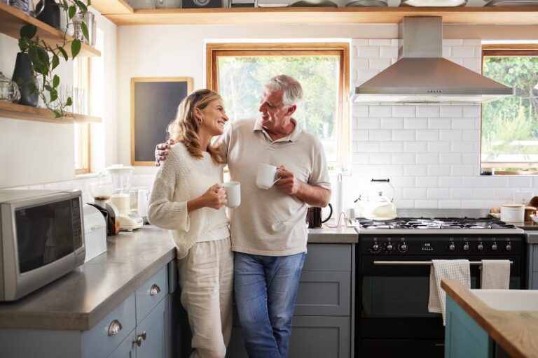 Senior, couple and drinking coffee with a love, marriage and happiness morning mindset at home. Happy smile and hug of a elderly woman and man with tea in a house kitchen together with quality time.
