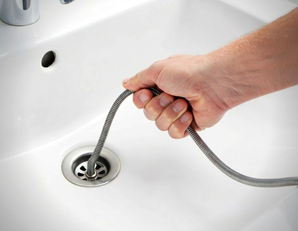 clogged drain deep in pipe hand holding snake to unclogg drain