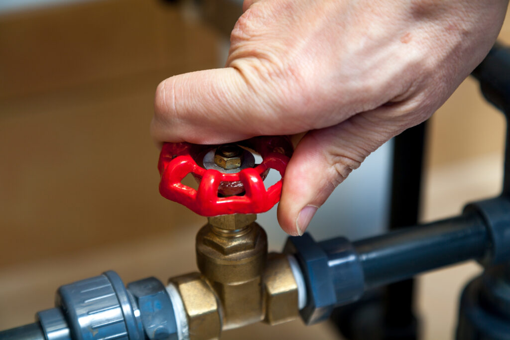 irrigation backflow preventer Hand turns the red round handle of a valve on a plastic pipe
