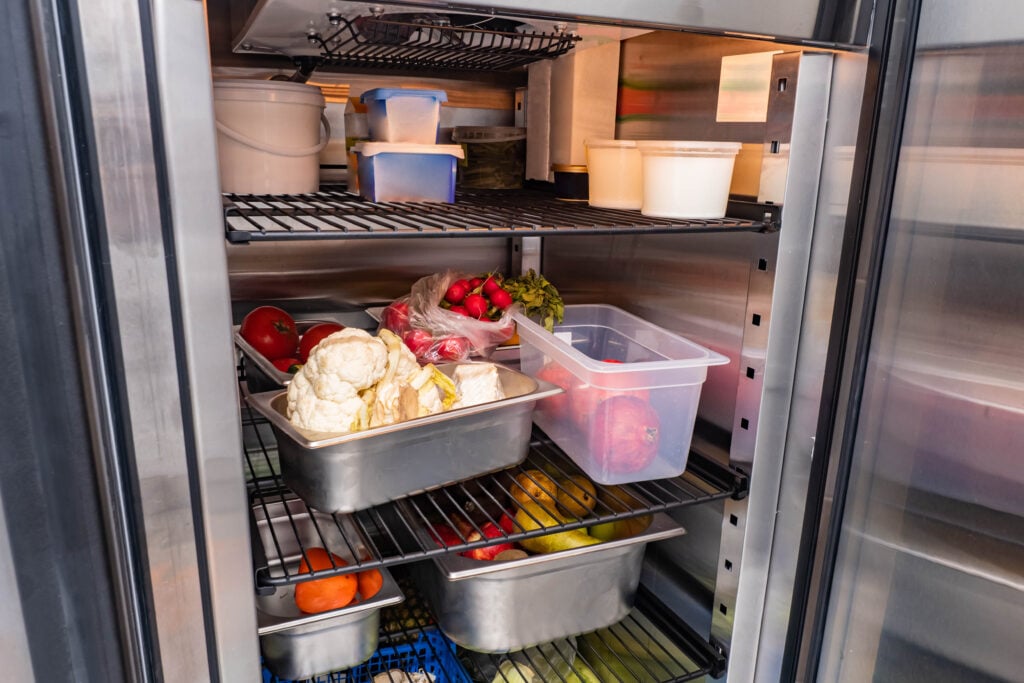 commercial refrigeration equipment Refrigerator of restaurant with food. Vegetables in restaurant refrigerator. Containers with vegetables on shelves of refrigerator. Radishes, cauliflower and pears in fridge camere.