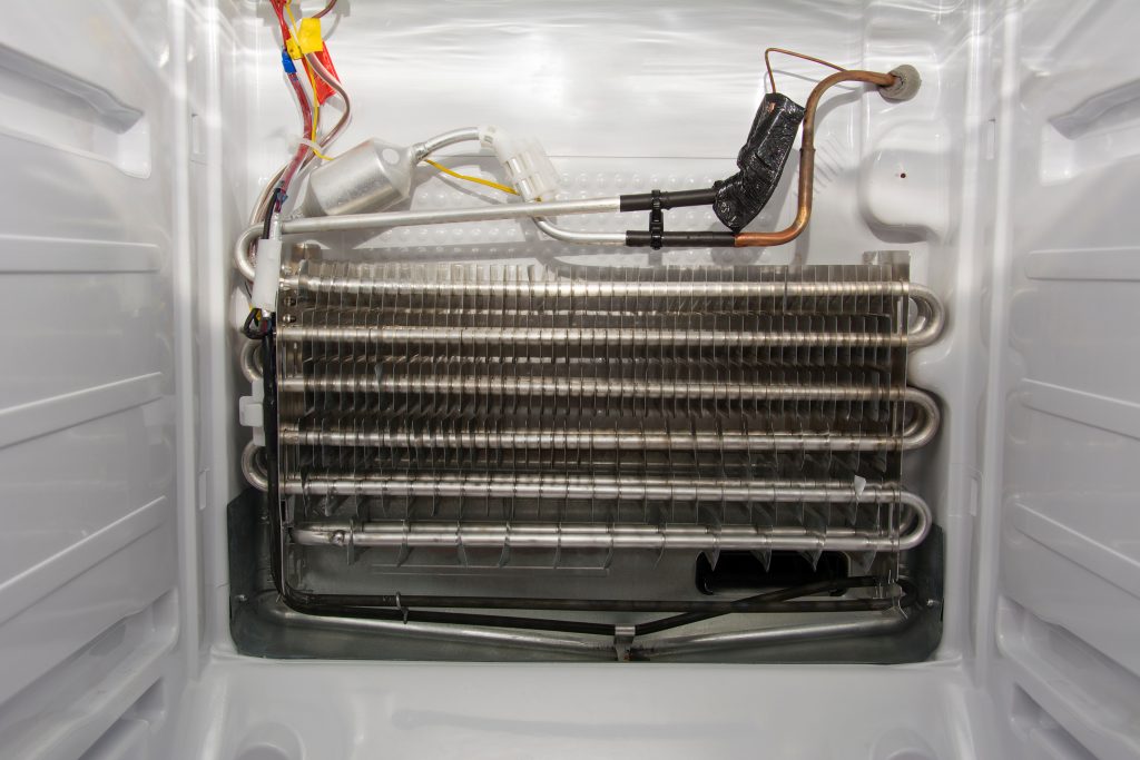 Disassembled white modern home freezer with stainless steel radiator, copper piping and sensor, inside view. Concept of maintenance and repair of refrigerators.